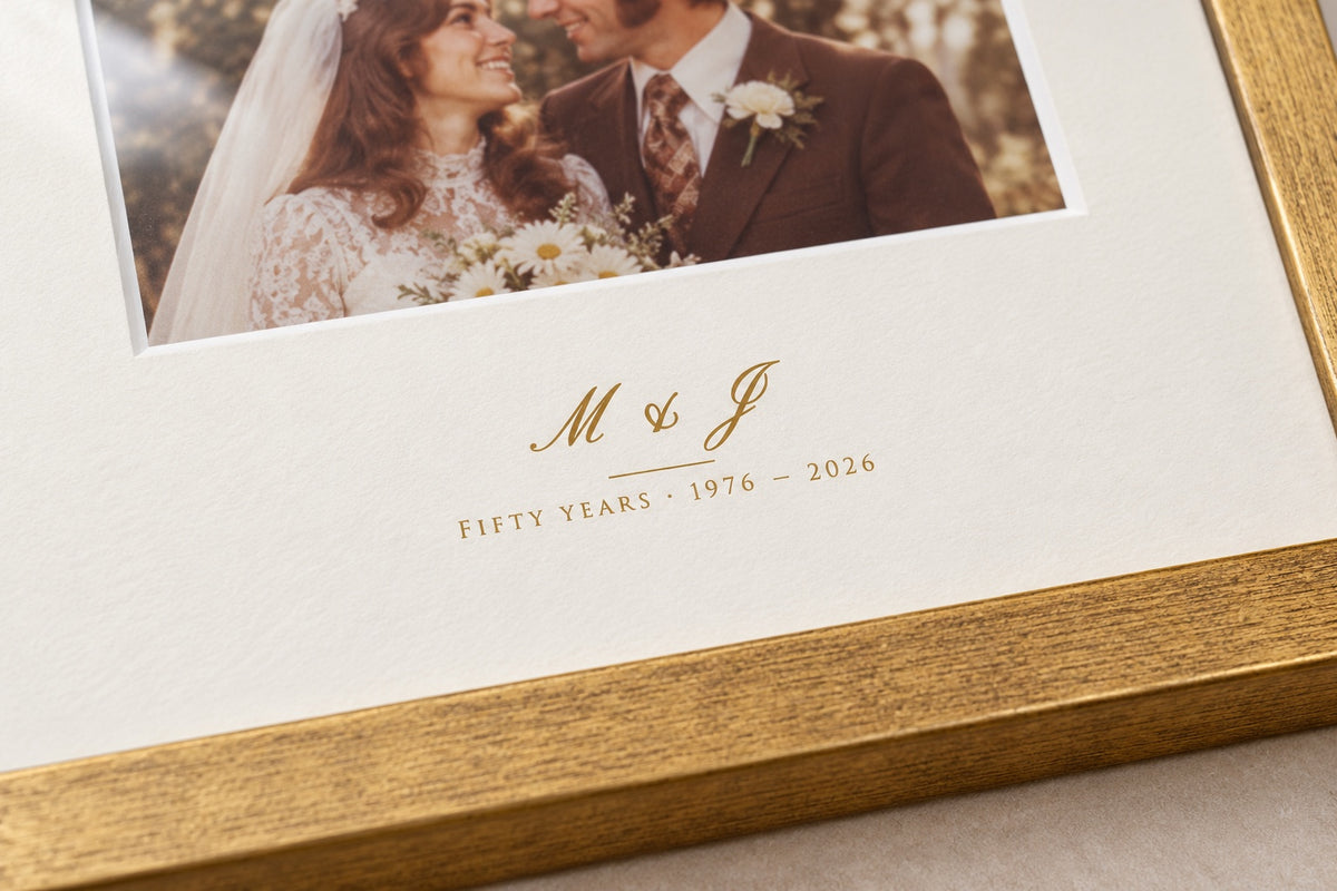 Close-up of the initials M & J and "Fifty years 1976 – 2026" printed in gold-tone ink on the mount