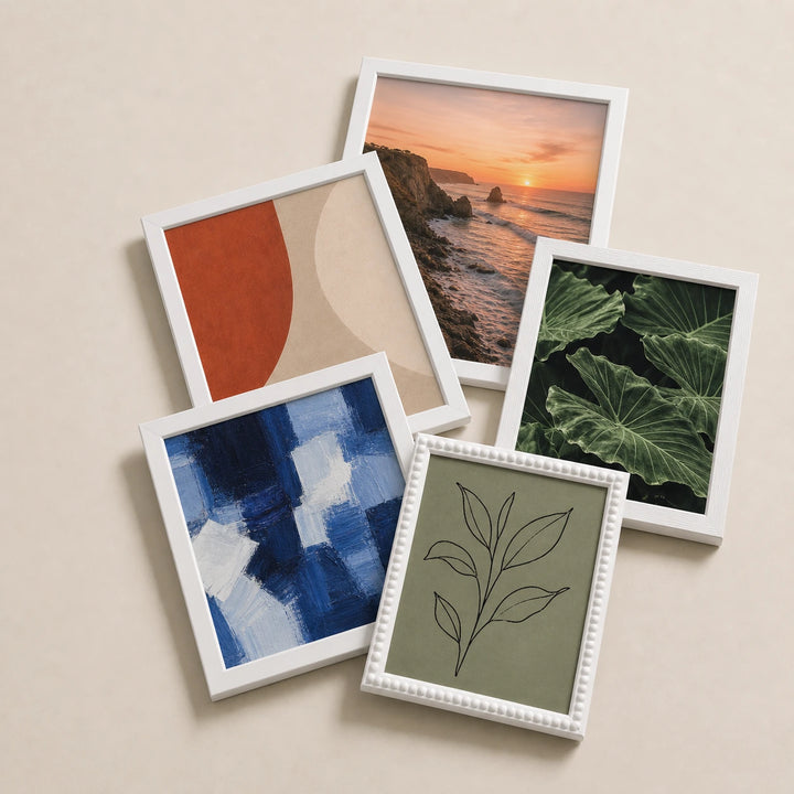 A collection of white picture frames lying flat with varied edge-to-edge artwork
